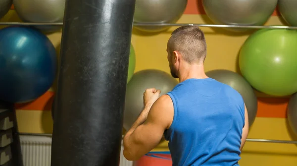 Muscular man in the gym. The man hit a punching bag, exercise. Boxing, workout, muscle, strength, power - the concept of strength training and boxing