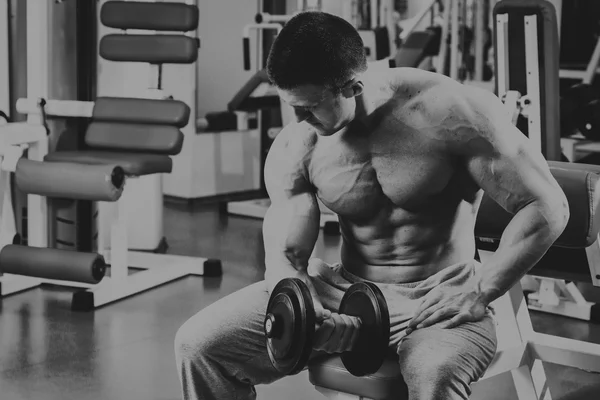 Bodybuilder makes exercise with dumbbells at the gym.