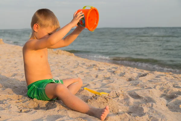 Boy shorts on the beach. Children playing with sea sand. Joy and fun for children. A beautiful warm day. Photo for children\'s magazines and websites.