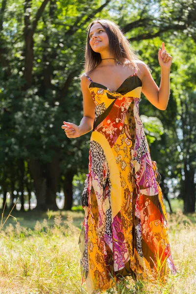 A young and attractive girl in beautiful summer dress middle of sunny meadows. Cheerful girl basking in the warm rays of the summer sun. Beautiful image of a carefree girl.