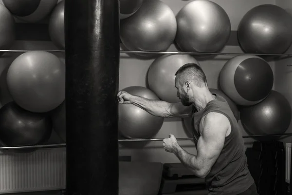 Muscular man in the gym. The man hit a punching bag, exercise. Boxing, workout, muscle, strength, power - the concept of strength training and boxing