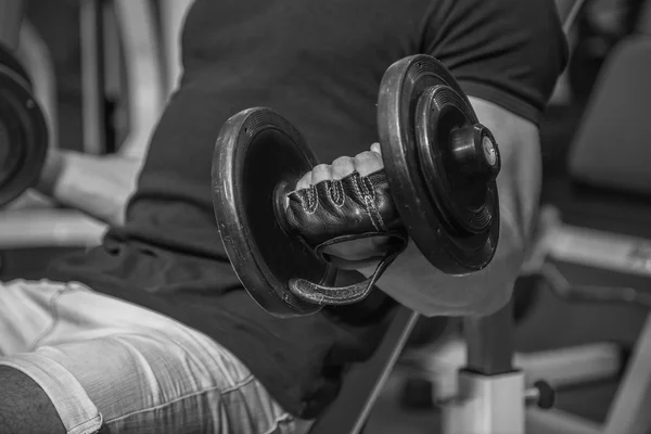 Bodybuilder makes exercise with dumbbells at the gym. Work on hands tell muscles. Exhausting workouts to an end. Photos for sporting magazines and websites.