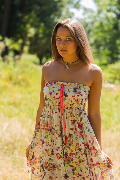 A young and attractive girl in beautiful summer dress middle of sunny meadows. Cheerful girl basking in the warm rays of the summer sun. Beautiful image of a carefree girl.