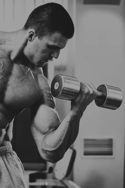 Bodybuilder makes exercise with dumbbells at the gym.
