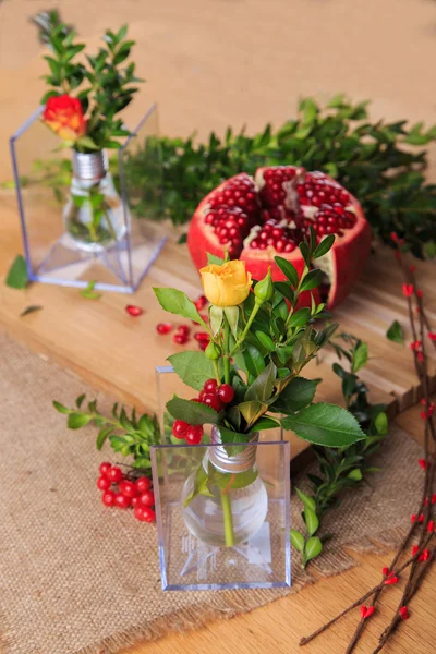 Beautiful composition with pomegranate, flowers and bulbs. Beautiful still-life with a pomegranate on the wooden background. Beautiful composition decor of fruits and flowers.