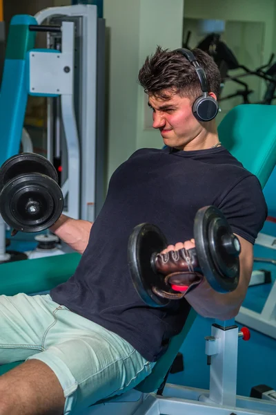 Bodybuilder makes exercise with dumbbells at the gym. Work on hands tell muscles. Exhausting workouts to an end. Photos for sporting magazines and websites.
