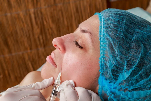 Cosmetic injection in the spa salon. Beautician makes injection into the patient's face.