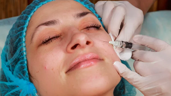 Cosmetic injection in the spa salon. Beautician makes injection into the patient's face.