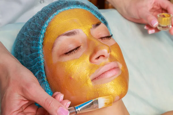 Application of golden masks on the face of the model. Cosmetic procedures