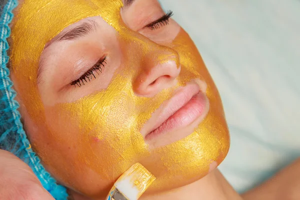 Application of golden masks on the face of the model. Cosmetic procedures