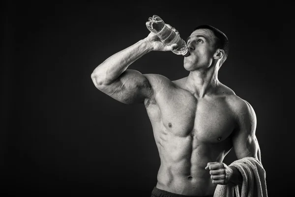 Muscular man on a dark background drinking water after workout