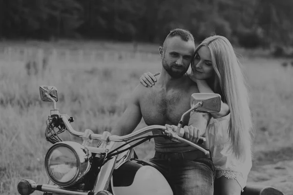 Muscular man with a beautiful woman on a motorcycle middle of a field road