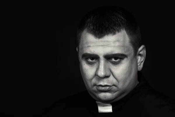 A professional stage actor in the guise of a priest against a dark background