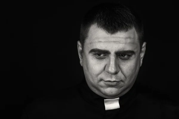 A professional stage actor in the guise of a priest against a dark background