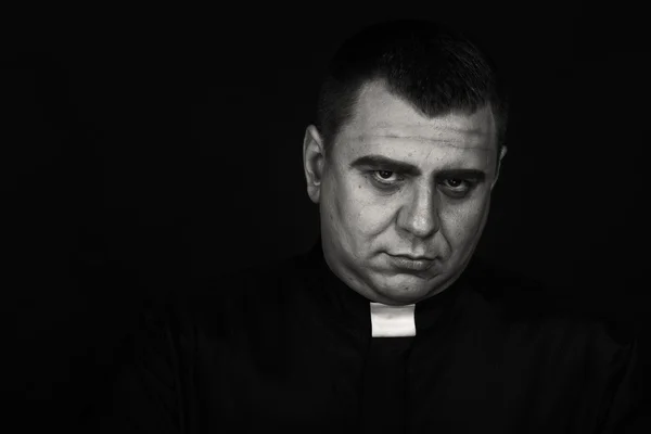 A professional stage actor in the guise of a priest against a dark background