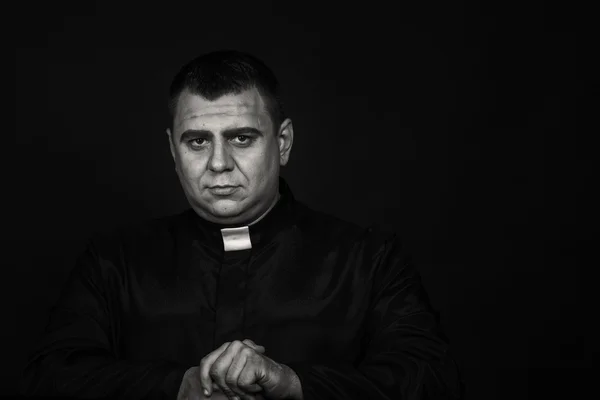 A professional stage actor in the guise of a priest against a dark background