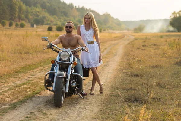 Muscular man with a beautiful woman on a motorcycle middle of a field road