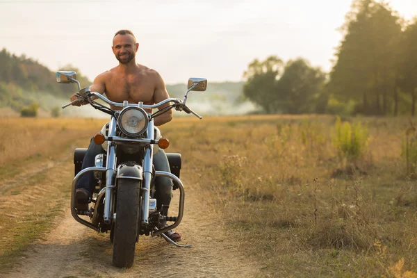 Muscular man with a beautiful woman on a motorcycle middle of a field road