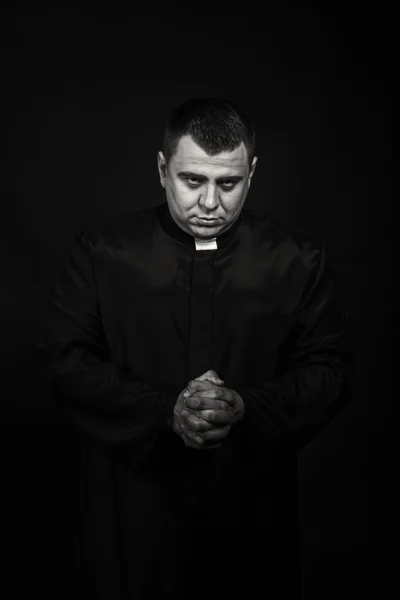 A professional stage actor in the guise of a priest against a dark background