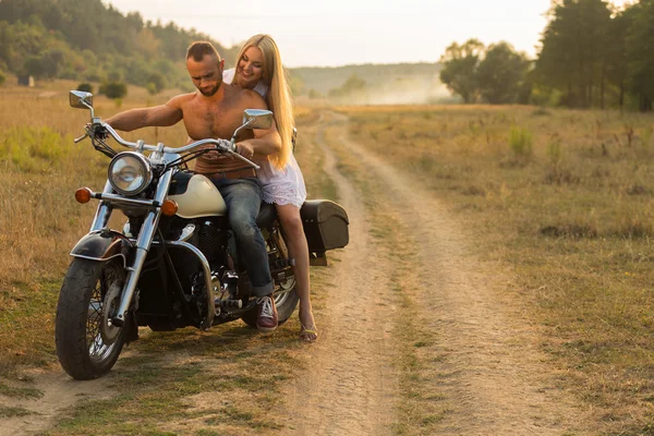 Muscular man with a beautiful woman on a motorcycle middle of a field road