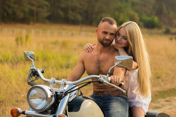 Muscular man with a beautiful woman on a motorcycle middle of a field road