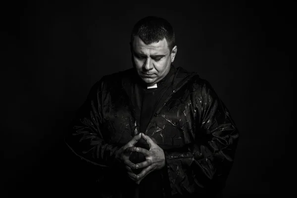 A professional stage actor in the guise of a priest against a dark background