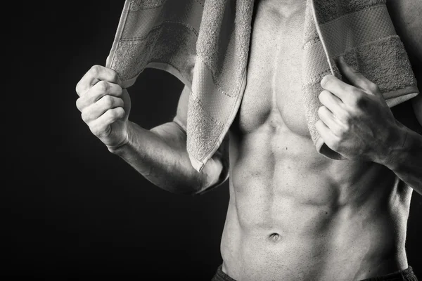 Muscular man with a towel in his hands on a dark background