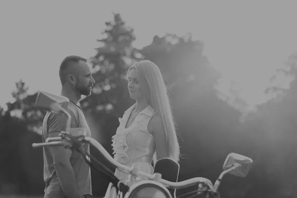 Muscular man with a beautiful woman on a motorcycle middle of a field road