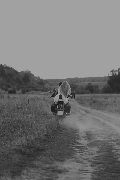 Muscular man with a beautiful woman on a motorcycle middle of a field road