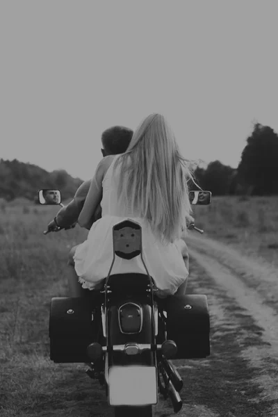 Muscular man with a beautiful woman on a motorcycle middle of a field road
