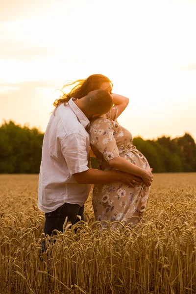 A young man and a pregnant woman sitting in a wheat field of freshly cut wheat
