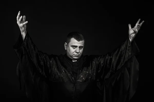 A professional stage actor in the guise of a priest against a dark background