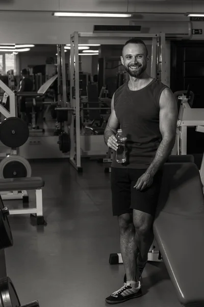A strong man in the gym. Rest between exercises. Handsome man drinks water.