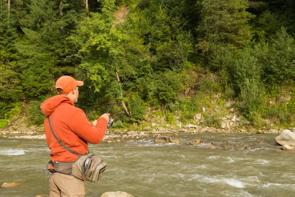 Young fisherman on a mountain river from spinning. Fishing in mountain rivers. Focusing on the process of catching and trade of fisherman. Photo for fishing and Natural magazines, posters, websites.