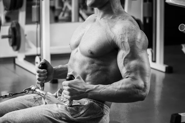 Strong muscular man doing exercises in the gym. Beautiful body on a black and white photo. Healthy lifestyle.