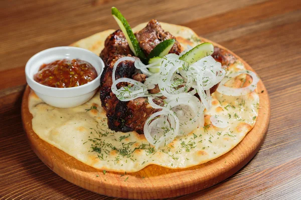 Appetizing barbecue cooked with vegetables and sauce served on a wooden tablet.