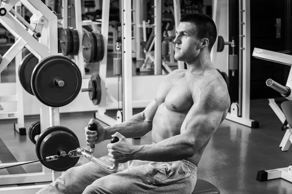 Strong muscular man doing exercises in the gym. Beautiful body on a black and white photo. Healthy lifestyle.