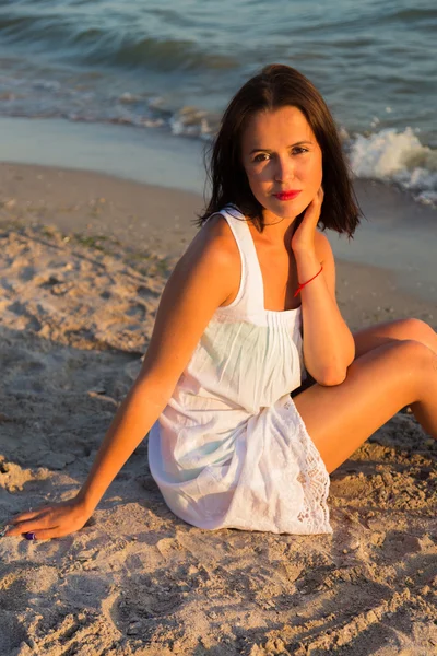 The young beautiful girl in a white dress on the beach. Photo beautiful girl on the beach. Girl posing in seductive manner. Photo for travel and social magazines, posters and websites.