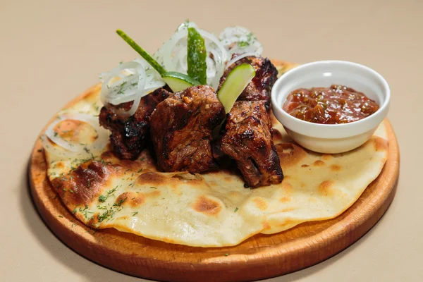 Appetizing barbecue cooked with vegetables and sauce served on a wooden tablet.