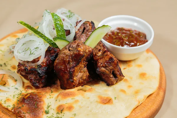 Appetizing barbecue cooked with vegetables and sauce served on a wooden tablet.