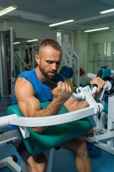 The athlete does bench biceps on the simulator in the gym. Hand muscle training on the simulator. Tense muscles of hands under load. Photos for sporting magazines, posters and websites.