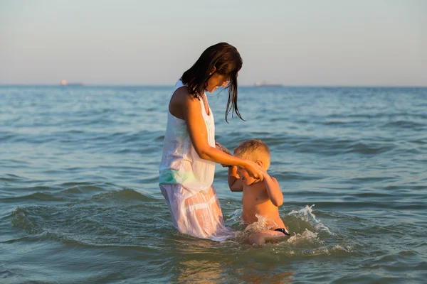 Young mother with son playing in the sea. A beautiful young mother and little boy happy gaming in water. Family holidays at sea. Photo for family and social magazines, posters and websites.