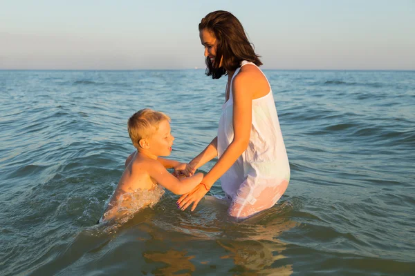 Young mother with son playing in the sea. A beautiful young mother and little boy happy gaming in water. Family holidays at sea. Photo for family and social magazines, posters and websites.
