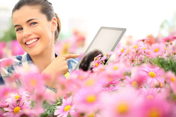 Woman with tablet smiling in garden flowers