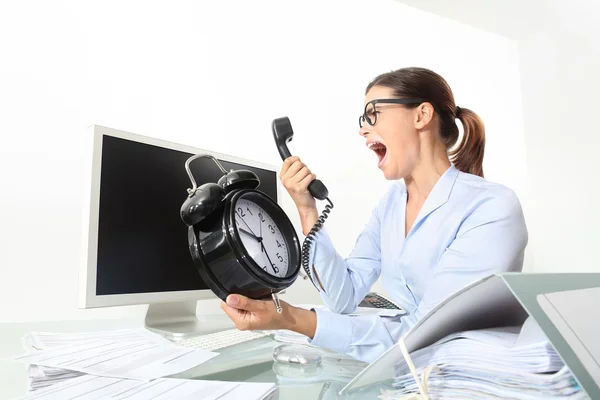 Angry woman at phone in office desk with clock, computer and doc