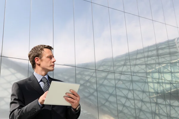 Businessman with tablet that looks far into the sky, in a scene of urban building with many glass windows