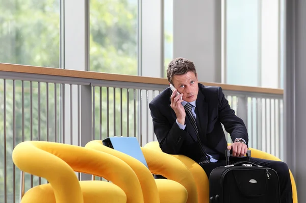 Travel business man talking on the phone, sitting with luggage, waiting room