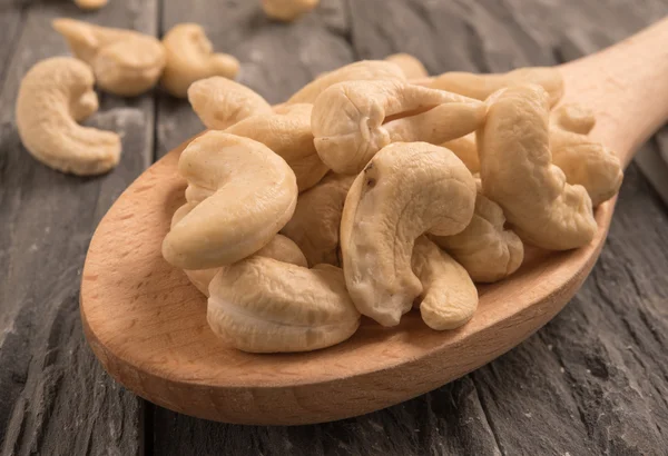 Cashew nuts in a wooden spoon on a black wooden background