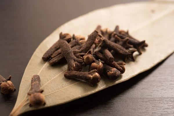 Cloves randomly arranged in dried Indian bay leaves on a black background