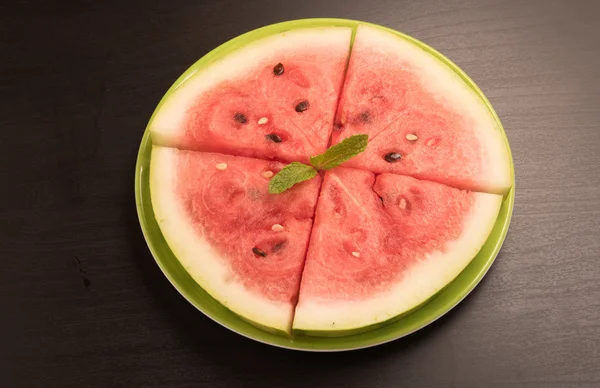 Sliced watermelon arranged in a green plate on black background